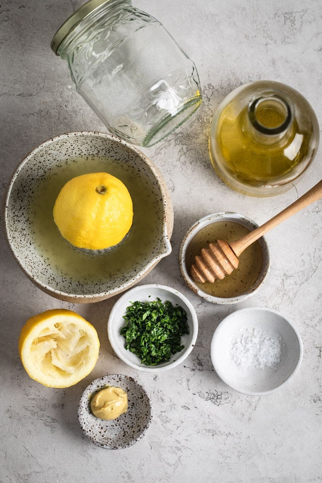 A jar of lemon and herb vinaigrette beside olive oil on a kitchen counter.